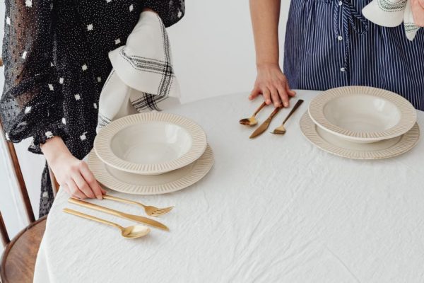 Two people setting a table with ceramic bowls and gold cutlery indoors.